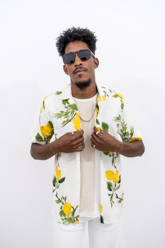 A vertical shot of a young Afro-American male in a floral shirt and sunglasses posing on a white background