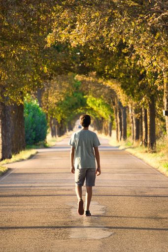 A vertical shot of aHispanic  boy walking down a path in the park