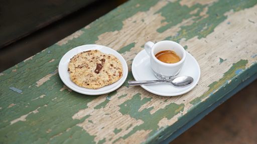 A clsoeup shot of a cookie with chocolates next to the coffee on the wooden surface