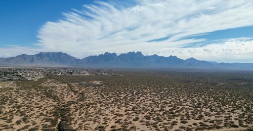 Aerial view of desert landscape with Organ Mountains under a partly cloudy sky in New Mexico.