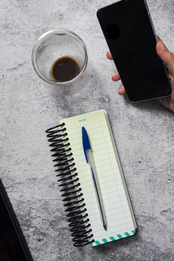 Top view of a to-do list notebook with a pen, smartphone, half-full coffee cup on a gray textured surface.