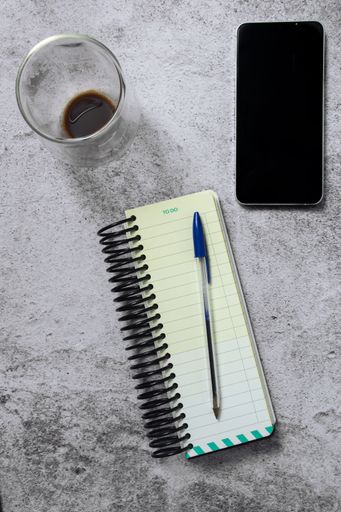 Top view of a notebook, pen, smartphone, and a half-full coffee cup on a textured surface, ideal for productivity themes.