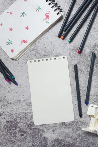 Top view of blank paper, notebook, and colorful pencils on a textured surface