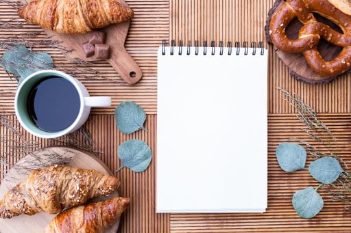 A top view of croissants with a pretzel and a cup of coffee on the table with a notepad on it