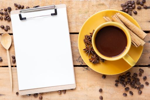 A top view of blank sheets of paper and a cup of fresh coffee on a wooden table