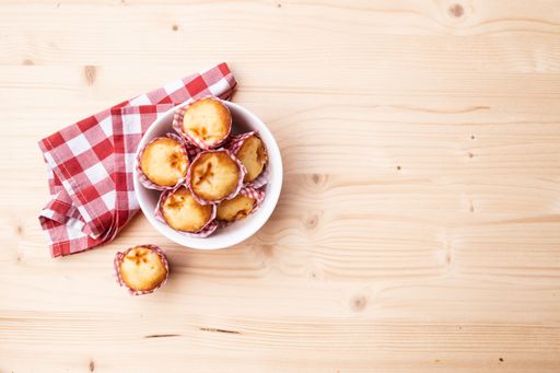 A top view of fresh muffins in a bowl on a wooden table with a napkin on it