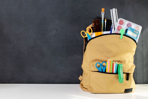 School backpack full of Stationery Supplies on blackboard with copy space ready for back to school season