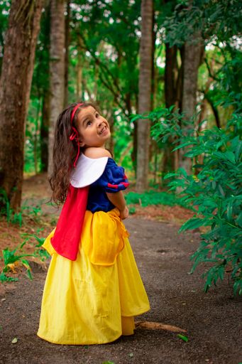 A cute little Hispanic girl wearing a Snow White dress as her Halloween costume in a forest