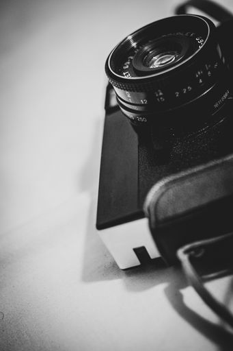 A vertical closeup of a film camera with focus on its lens in grayscale