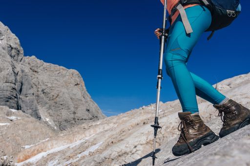 Close up shot of a woman wearing trekking or hiking boots, leggins and using trekking poles. Outdoor shoes on a rock with mountains in background.