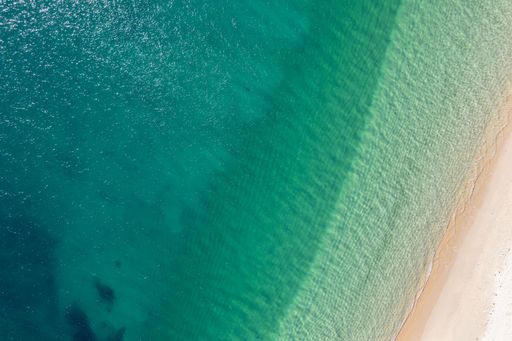 zenithal aerial view of the shore of a white sandy beach with turquoise waters, textured background for summer concept