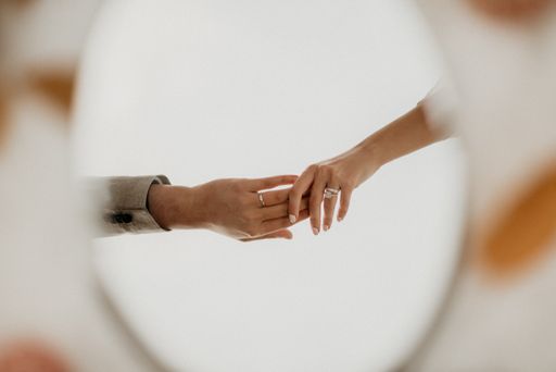 A selective focus shot of hands with wedding rings on it in a reflection of a mirror