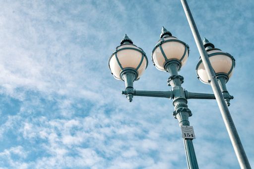 A vintage street lamp set against a partly cloudy blue sky, capturing an urban architectural detail.