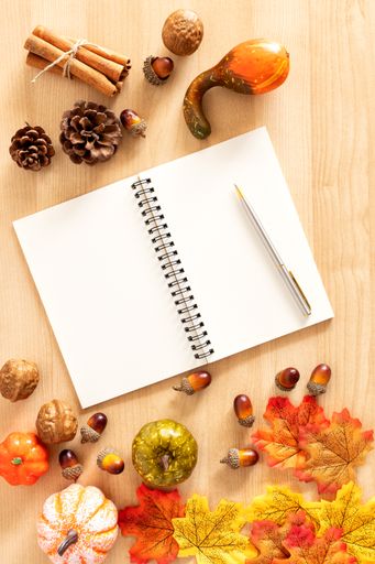 A top view shot of a wooden table with thanksgiving decors, a notebook, and a pen