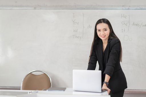 A female teacher in a black business suit and with a laptop in a classroom