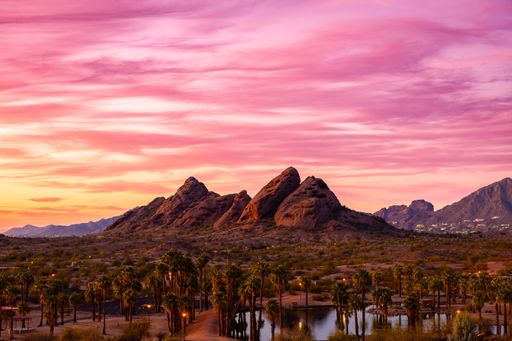 A vibrant sunset over Papago Park in Phoenix, Arizona with red rock formations and palm trees under a pink and orange sky.