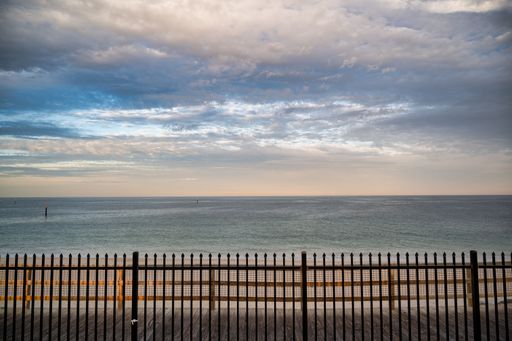 A serene ocean view with a metal fence in the foreground and a cloudy sky above, capturing the calmness of the sea.
