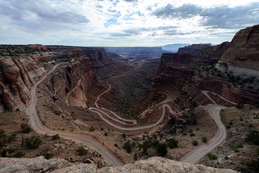 A breathtaking view of a winding dirt road through a canyon landscape in Canyonlands National Park under a partly cloudy sky.