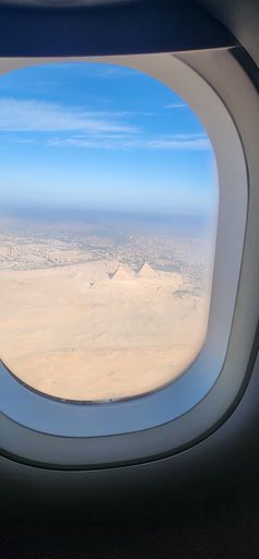 Aerial view of the Pyramids of Giza through an airplane window, under a clear blue sky, showcasing the iconic Egyptian landscape.