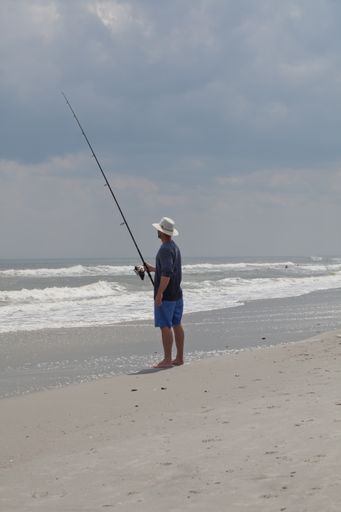 A person wearing a white hat surf fishing at Myrtle Beach South Carolina