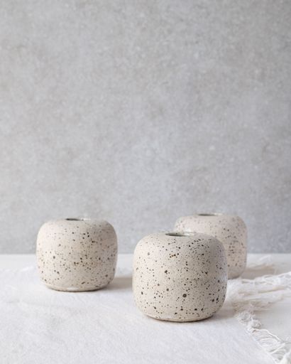 Three small, round vases with a speckled texture sit on a light surface against a textured grey background.