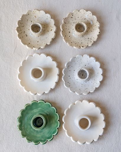 Six scalloped candle holders in varying colors and textures are arranged on a neutral surface.