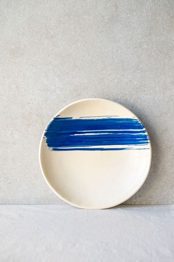 A white ceramic plate features a bold, horizontal blue brushstroke design.