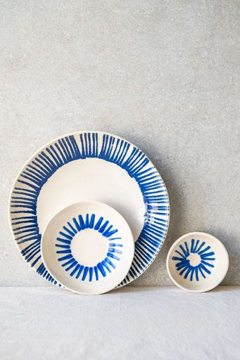 Three white ceramic dishes with a hand-painted radiating blue burst design are arranged against a neutral backdrop.