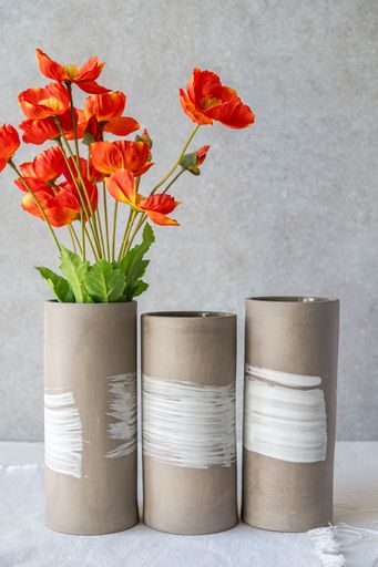 Three cylindrical vases, two with white painted details, hold a vibrant bouquet of orange flowers.