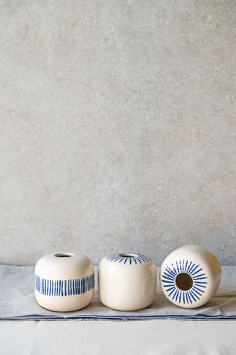 Three round, white clay vases with blue stripes are arranged on a light surface.