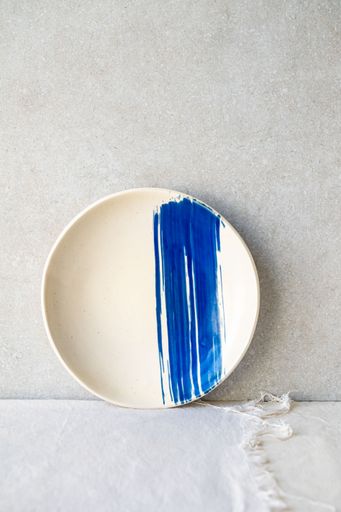 A white ceramic plate features a bold, horizontal blue brushstroke design.