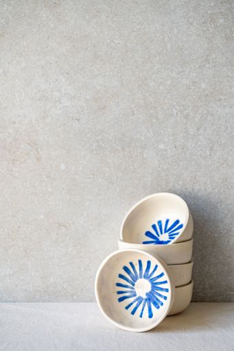 A stack of small, white ceramic bowls with a radiating blue design sits against a neutral backdrop.