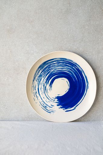 A white ceramic plate features a bold, circular blue swirl design.