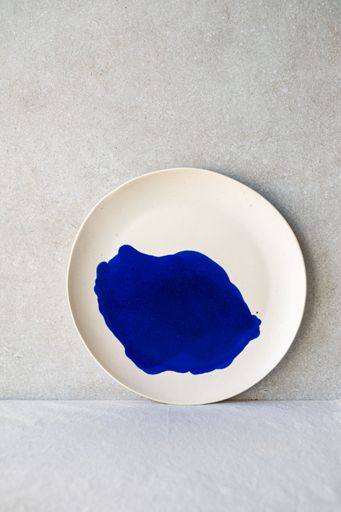 White plate with a vibrant blue paint splatter on it.