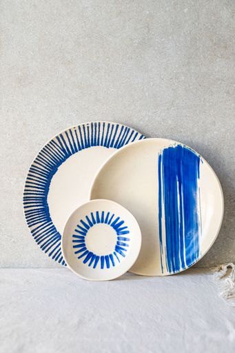 Three white ceramic plates, each with a unique blue hand-painted design, are arranged against a neutral backdrop.