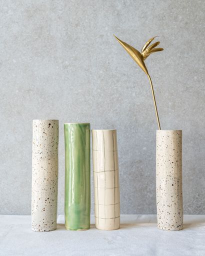 Four cylindrical vases, made of stone or ceramic with varying textures and colors, stand against a neutral background.