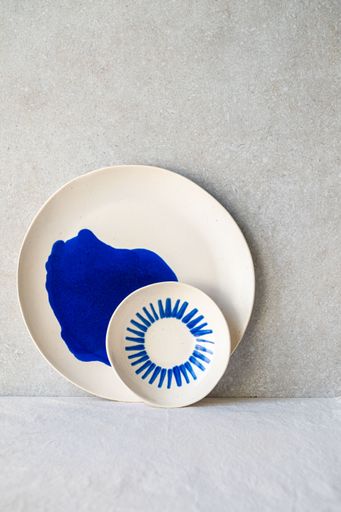 Two white ceramic plates, one with a bold blue abstract shape and the other with a radiating blue line design.