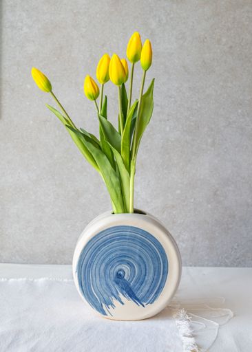 A modern ceramic vase with blue patterns holding vibrant yellow tulips against a neutral background.