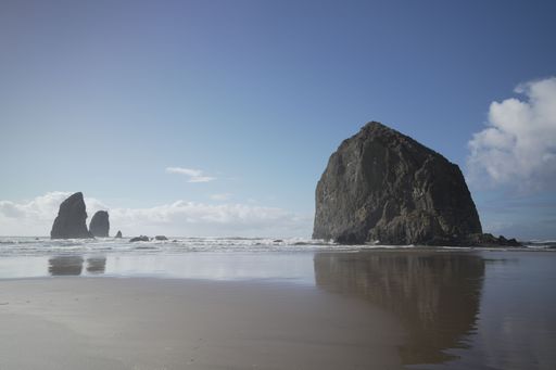 A scenic view of Haystack Rock at Cannon Beach, Oregon, with clear blue sky and ocean reflections.