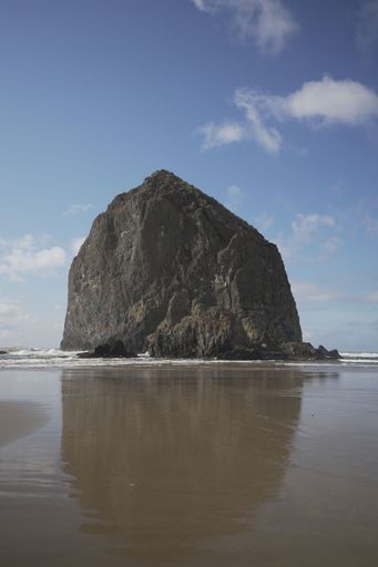 A scenic view of Haystack Rock at Cannon Beach, Oregon, with clear blue sky and ocean reflections.
