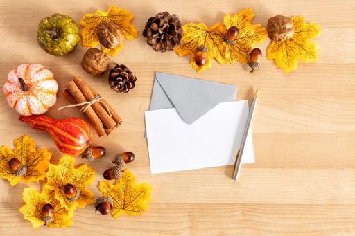 A top view shot of a wooden table with thanksgiving decors, envelopes with copy space, and a pen