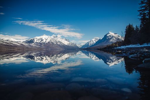 A stunning reflection of snow-capped mountains on a tranquil lake under a clear blue sky in Glacier National Park.