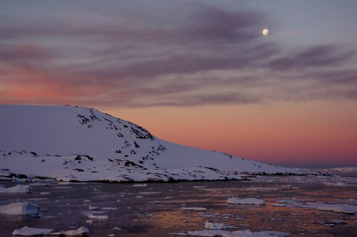 A serene Arctic landscape with snow-covered hills and a colorful sunset sky reflecting on icy waters.