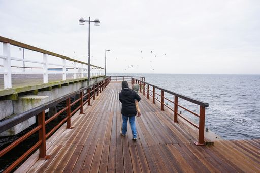 A woman and child walking on a wooden pier at the coast on a cloudy day