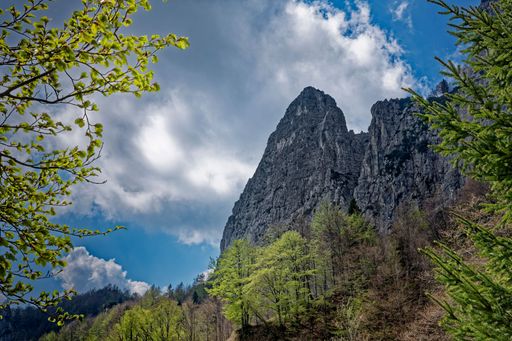 Scenic view of a rocky mountain peak surrounded by lush greenery under a cloudy blue sky, capturing the essence of nature's beauty.
