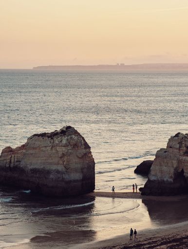 Scenic view of Praia da Rocha beach at sunset with people walking along the shore, featuring large rock formations and a calm sea in Algarve, Portugal