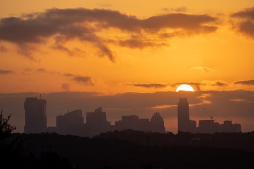 Silhouette of a city skyline at sunset with a vibrant orange sky and scattered clouds, capturing the urban landscape in a serene moment.