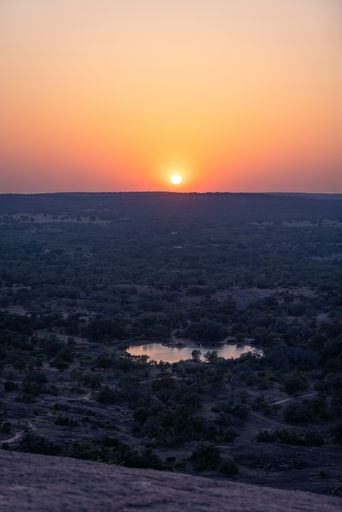 A serene sunset over a lush landscape with a small lake, capturing the vibrant colors of the sky.