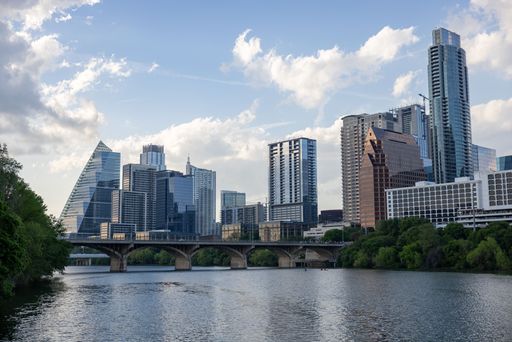 Austin skyline with modern skyscrapers and a bridge over the Colorado River under a partly cloudy sky.