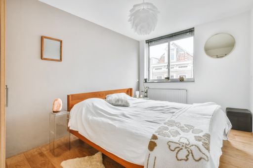 An interior shot of a bedroom in white walls and a wooden floor next to a window